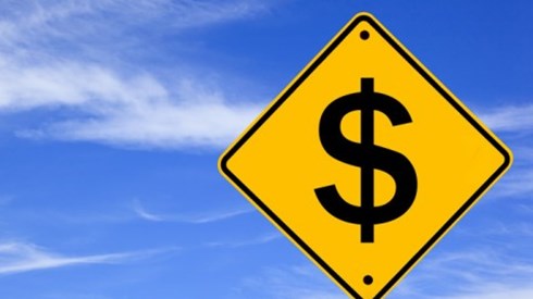 Yellow diamond-shaped traffic warning sign showing a dollar sign with a blue sky background.