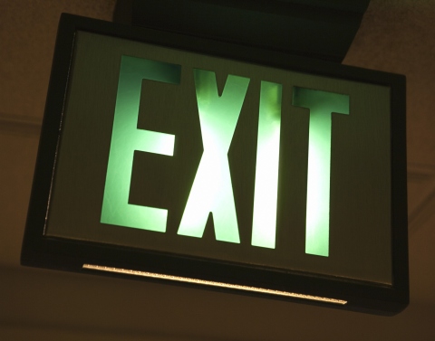 A green and white lit up EXIT sign mounted in a black frame on a ceiling