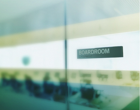 A glass conference room with the word BOARDROOM visible on the door and blurred interior of the room