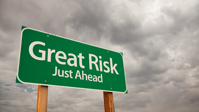 A green road sign that says "Great Risk Just Ahead" against a cloudy sky 