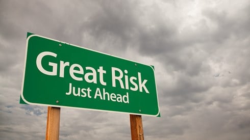 A green road sign that says "Great Risk Just Ahead" against a cloudy sky