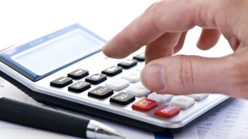 Hand using calculator resting on paper with numbers and pen next to it