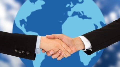 Two business professionals shake hands with a globe in the background