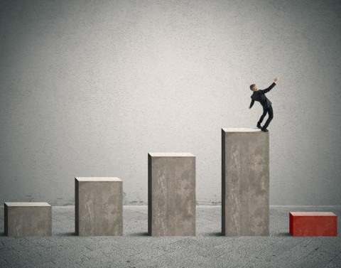 Businessman on top of a bar chart about to fall onto a low red bar at the end