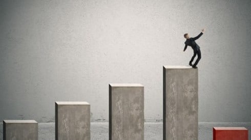Businessman on top of a bar chart about to fall onto a low red bar at the end