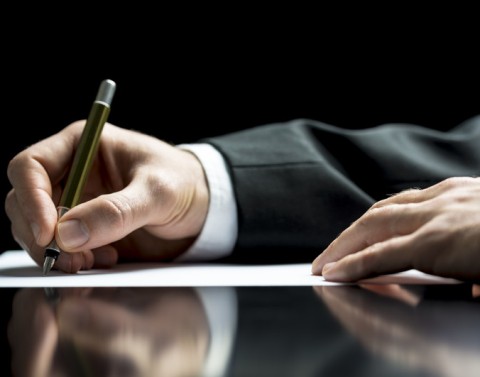 A businessman's hand holding a pen and writing a letter