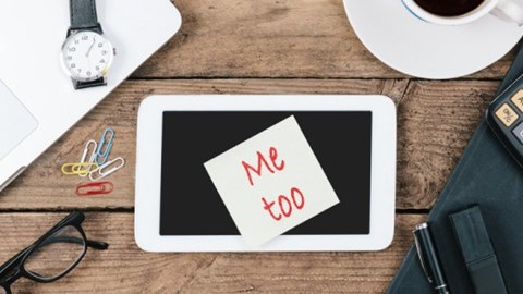 On a table there are eyeglasses, a watch, a cup of coffee, a calculator and a tablet with a note on top saying Me Too