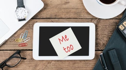 On a table there are eyeglasses, a watch, a cup of coffee, a calculator and a tablet with a note on top saying Me Too