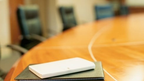 A round wooden conference table with black executive chairs around it and small black and white notebooks in one spot