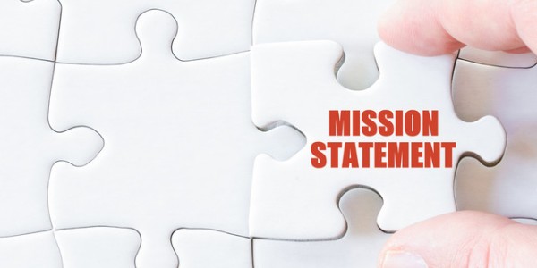 Two fingers are inserting the last piece of a puzzle that has written in red MISSION STATEMENT.