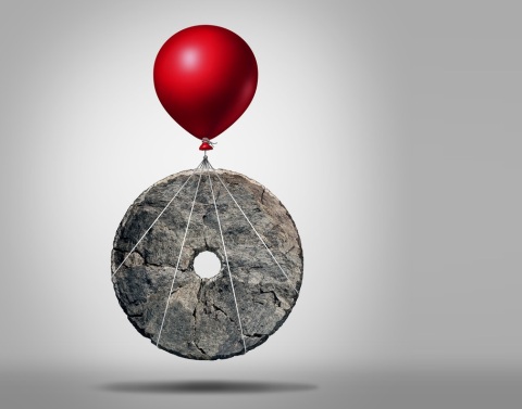 Red helium balloon attached to and lifting an ancient millstone