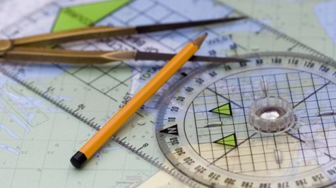 Navigational course plotting tools with compass and pencil laying on top of a map