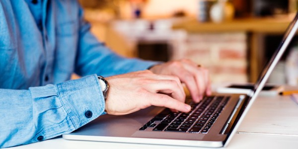 A male in casual clothing is in a home typing on a laptop.