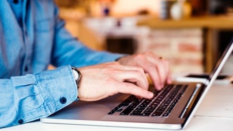 A male in casual clothing is in a home typing on a laptop.