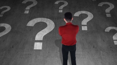 A man is standing and thinking while looking at a floor painted with large question marks