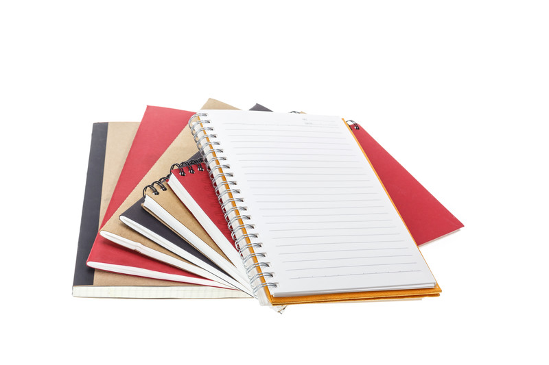 Several bound and sprial notebooks spread out on a white background with lined paper showing on top