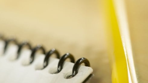The corner of a black spiral bound notebook on an indistinct yellows background