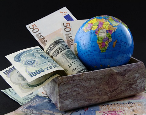 Box stuffed with dollars, yen, and euros and a globe sitting on top of other currencies