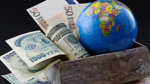 Box stuffed with dollars, yen, and euros and a globe sitting on top of other currencies