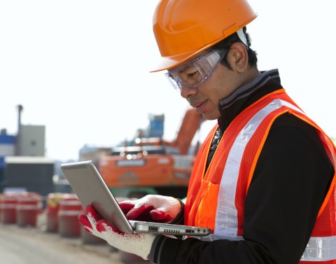 Construction Worker Using Laptop with Excavator in Background
