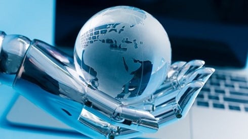 Robot hand holding globe in palm with computer screen in background