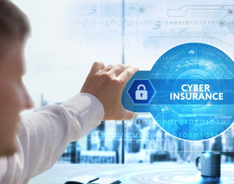 Man holding virtual blue safe with lock icon and dial and the words CYBER INSURANCE in glass above a desk in an office