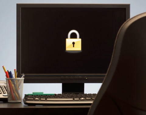 An office with a black computer monitor screen with a bright yellow lock, pencils, keyboard, phone, and chair