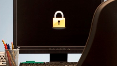 An office with a black computer monitor screen with a bright yellow lock, pencils, keyboard, phone, and chair