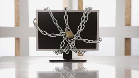 An office with a computer monitor on white desk with chains around it and locks attached to the chains on the front and back