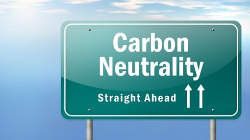 Green road sign reading 'Carbon Neutrality Straight Ahead' in front of blue sky