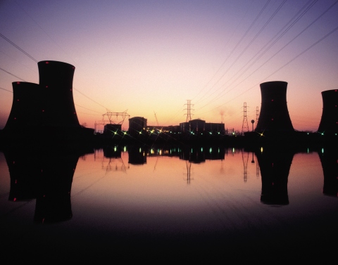 Nuclear power plant located on waterfront with evaporation silos and plant reflecting in water at sunset