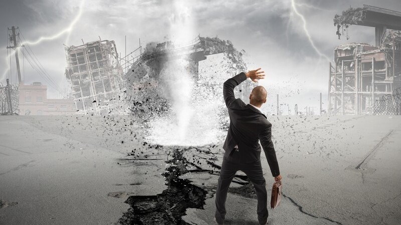 A businessman standing in front of a tornado and lightning strikes, shielding his face