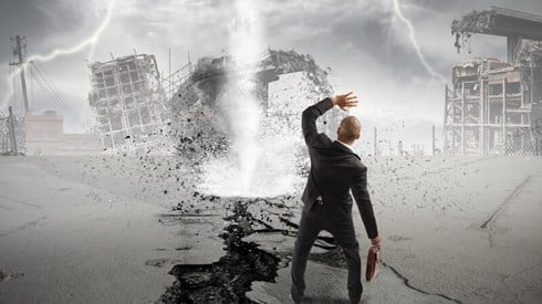 A businessman standing in front of a tornado and lightning strikes, shielding his face