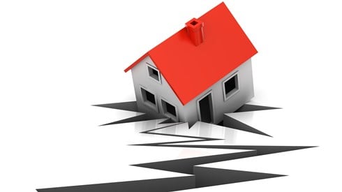 A crack in the ground from an earthquake with a house falling into it