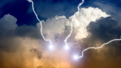 Blue sky with white and orange storm clouds emitting three white lightning bolts