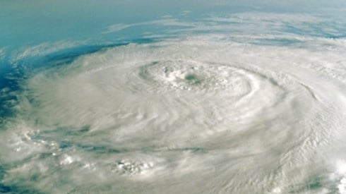An aerial view looking down on swirling white hurricane clouds and storm with blue ocean below