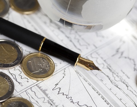 Euros scattered on a piece of paper with graphs showing trendlines and a black fountain pen and glass globe next to it