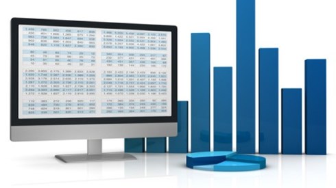 Large bar graph and pie chart figurines alongside a computer monitor with statistical data on the screen
