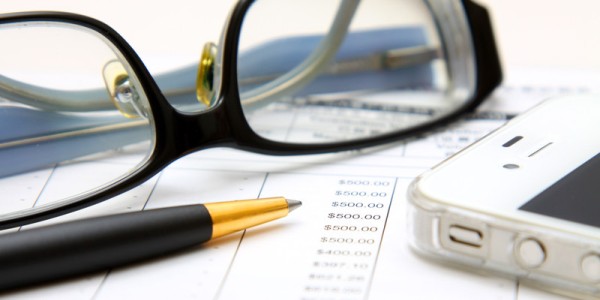Financial statement under review with eyeglasses, black and gold pen, and smartphone on top