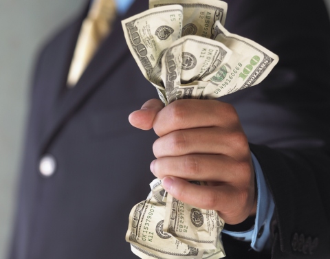 A businessman in a blue suit holding three crinked one hundred dollar bills and one fifty dollar bill
