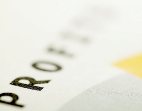 The word PROFIT in black type on white paper with the end of the word blurred and a yellow sticky note on the bottom