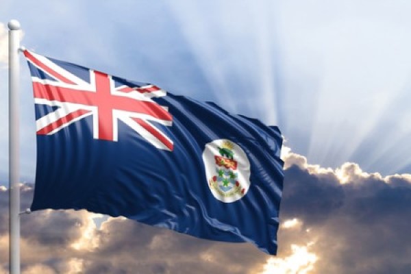 The flag of the Cayman Islands flying in a sunbeamed sky
