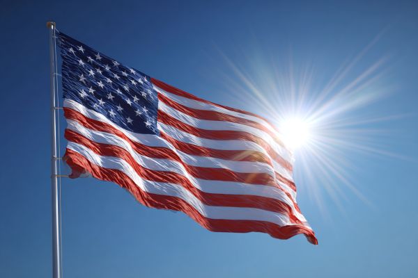USA flag flying in the blue sky in front of the sun