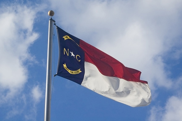 Flag of the State of North Carolina Flying on Flagpole Against Blue Sky with Clouds