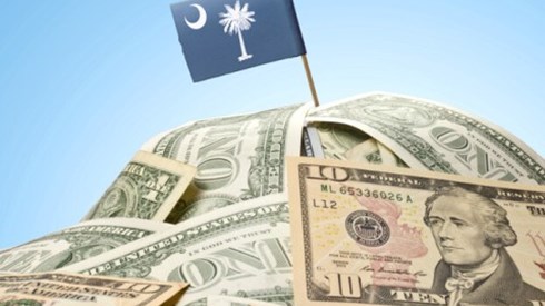 A hill-like stack of 1- and 10-dollar bills with a tiny flag pole and the South Carolina State Flag