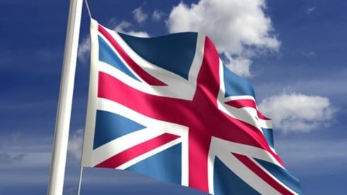 The United Kingdom flag on a flag poll waving in front of a blue sky with clouds