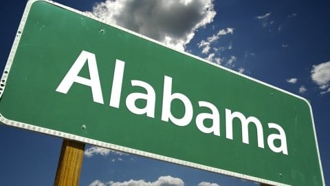 Green road sign with Alabama written on it and a blue sky with clouds in the background.