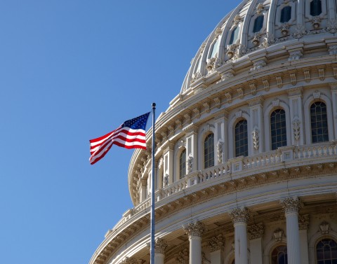 Close up of top portion of Capitol building with United States flag flying on a pole and blue sky in background