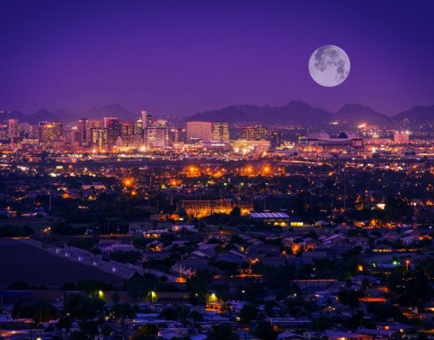 Nighttime city overview of Phoenix, Arizona, with mountains and large full moon in background