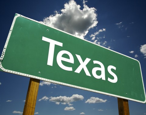Green road sign of Texas in front of blue sky with clouds
